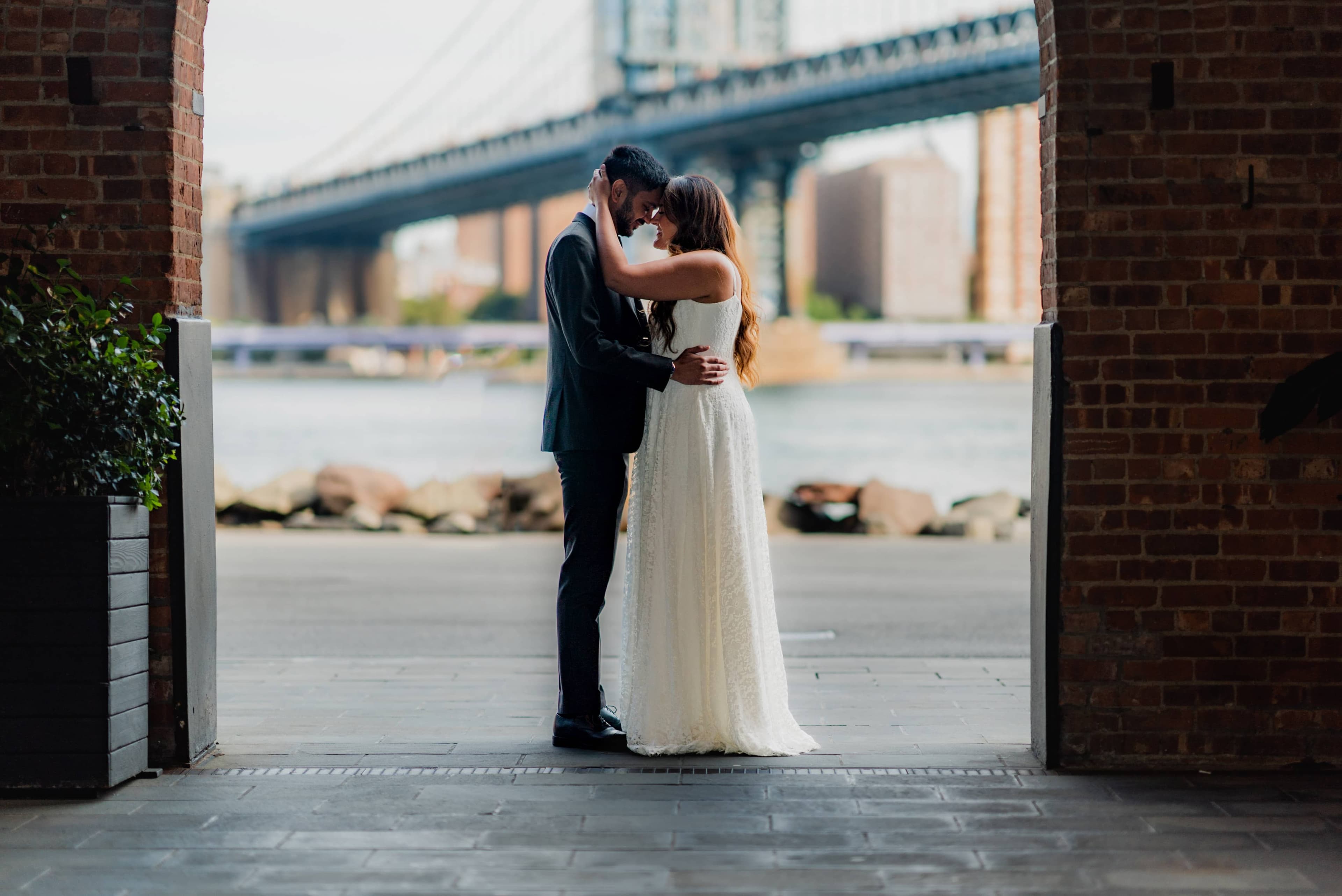 Wedding couple embracing by the waterfront beneath the Manhattan Bridge